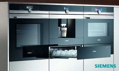 Offene Küche mit gedecktem Tisch, sechs Personen beim Abendessen, moderne Geräte im Hintergrund.